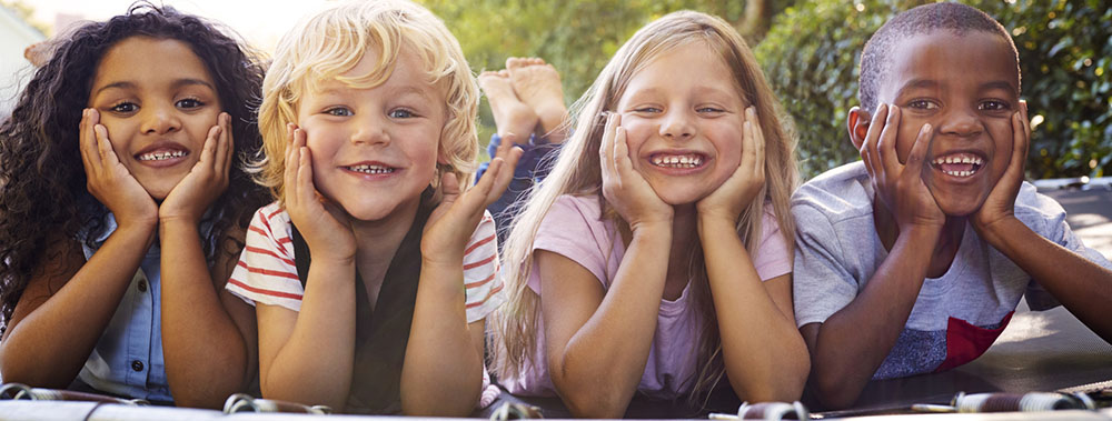 Four kids lying down together on a trampoline in the garden