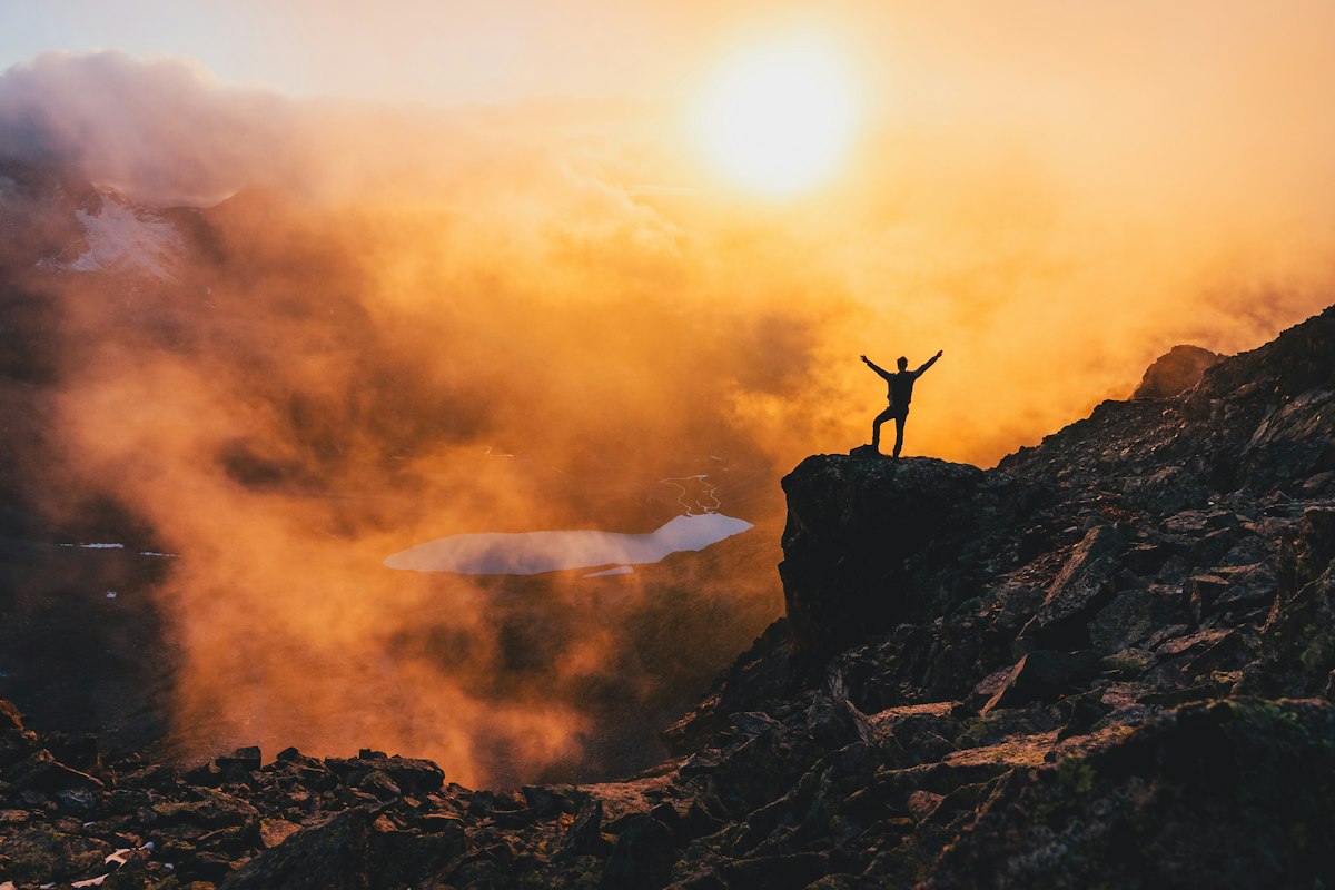 A hiker with arms raised on a mountain at sunrise