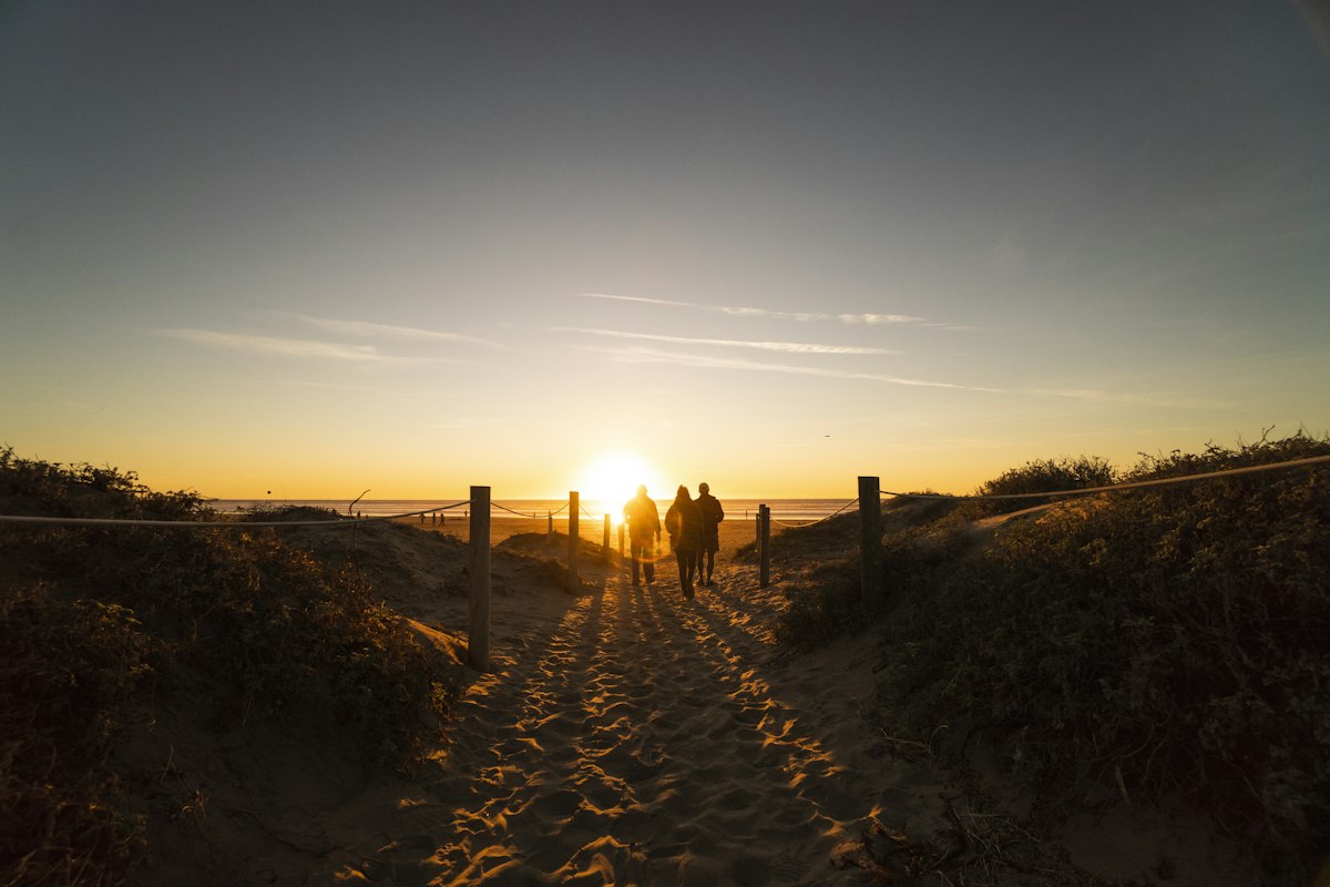 People walking a sandy path toward the rising sun