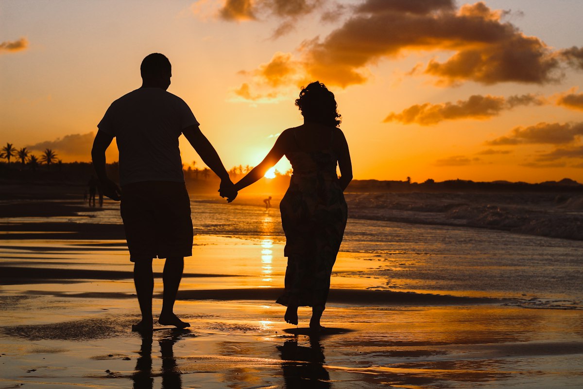 A couple holding hands on the beach at sunset