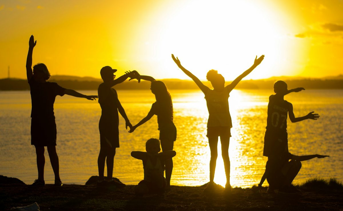 Friends silhouetted against a golden sunset with arms raised