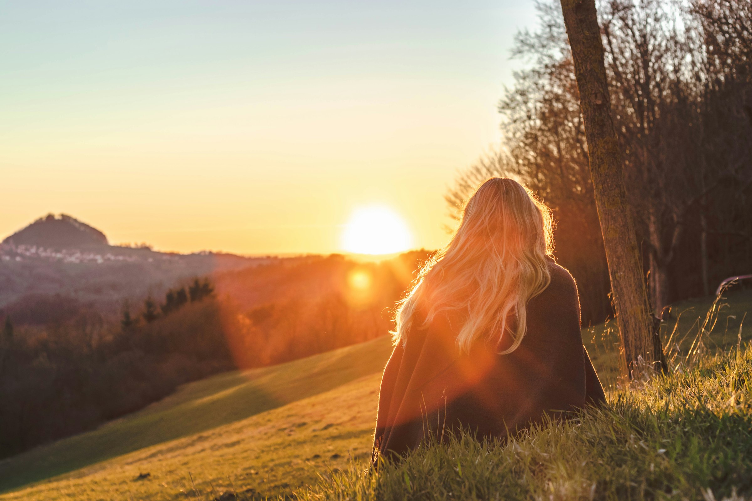 A woman sitting on a hillside watching the sunrise
