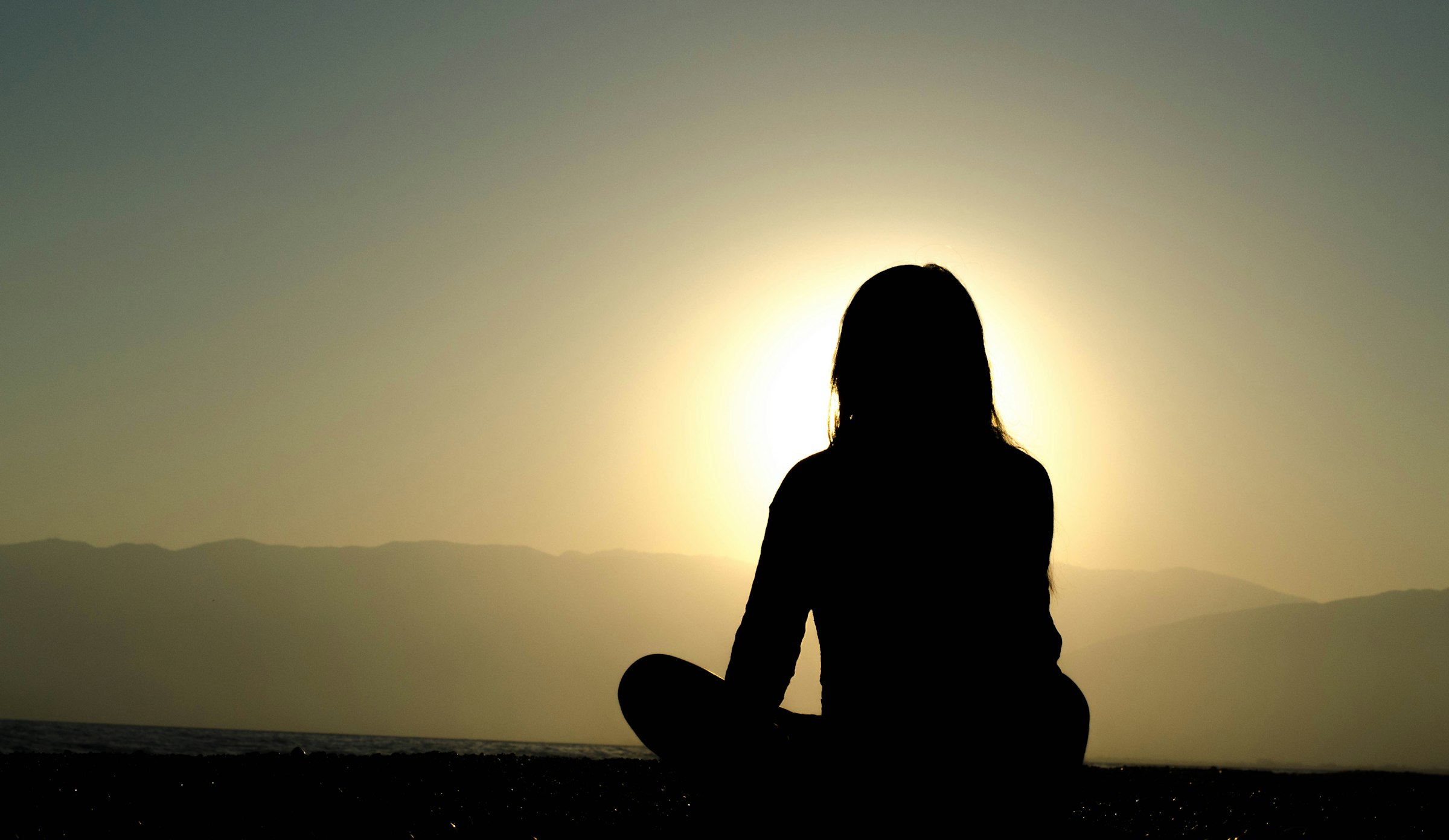 Silhouette of a woman meditating in front of the rising sun